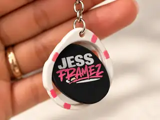 Personalized white and pink Jess Framez spinner keychain with a black rotating logo disc, centered in a hand-held photograph