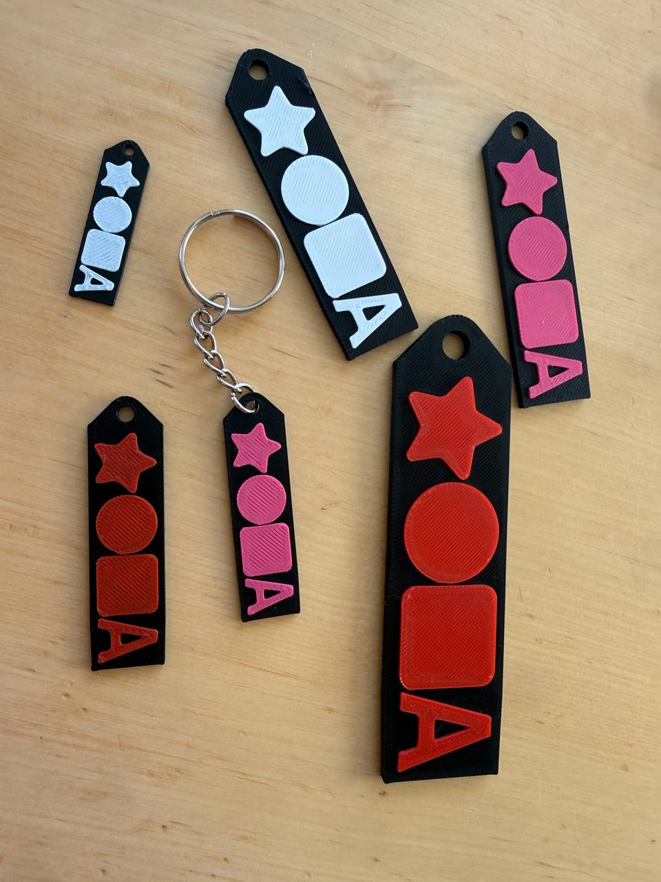 A set of real 3D-printed black keychains in different sizes with colorful raised star, circle, square and letter designs