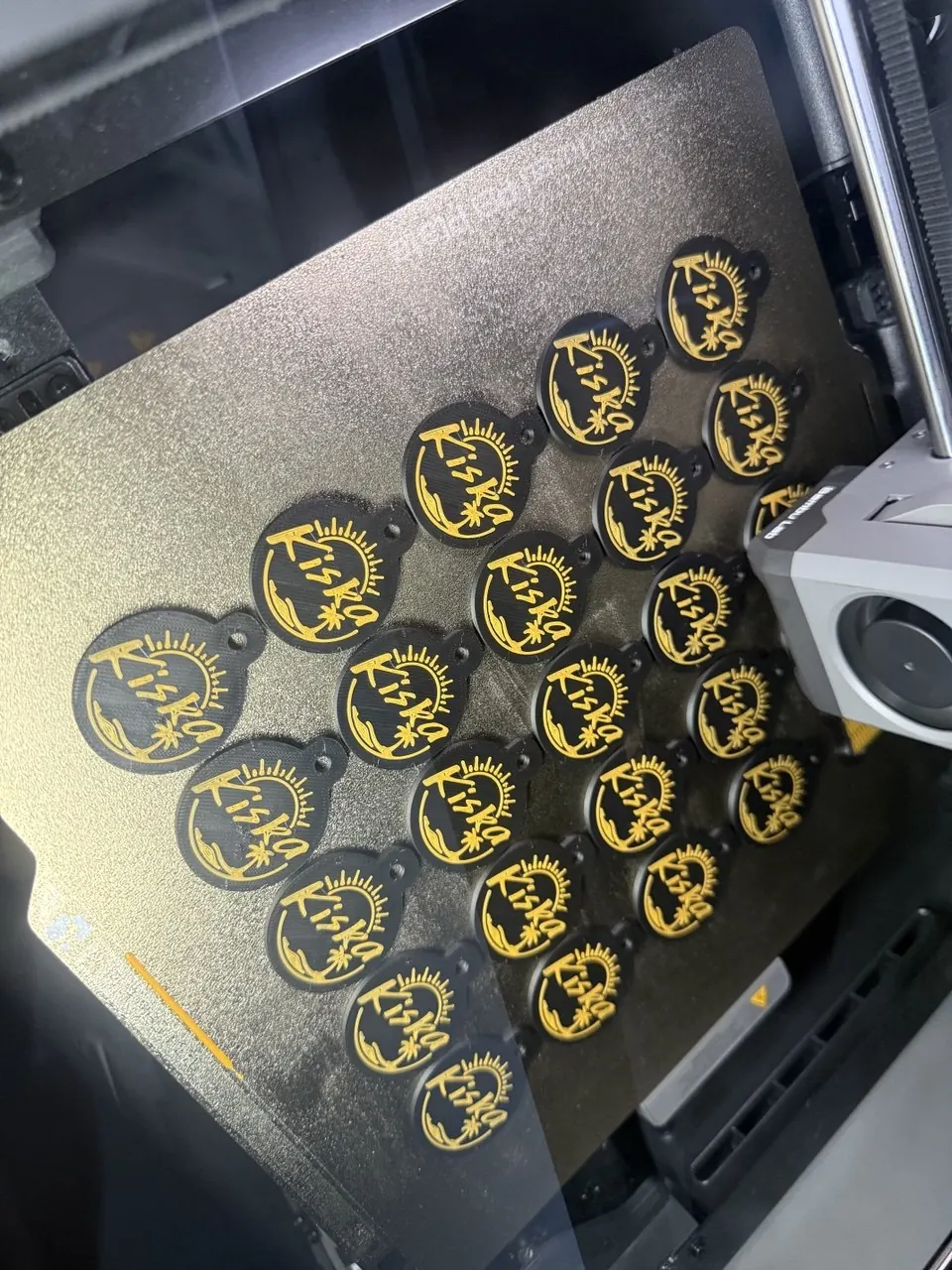 Black and yellow Kiska café keychains in a freshly printed batch on the build plate